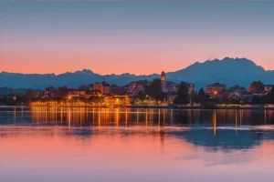 Tramonto romantico sul Lago Maggiore con borgo illuminato e montagne sullo sfondo